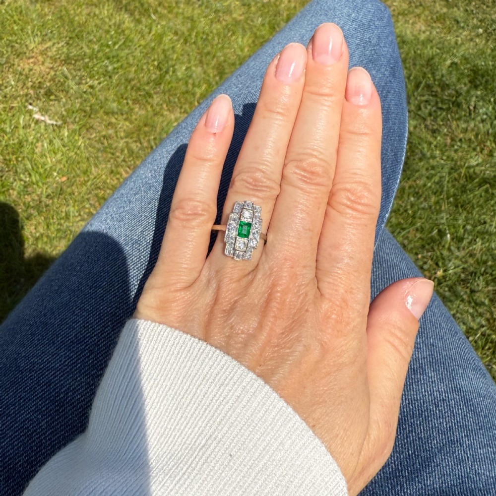 An Art Deco platinum ring featuring a central rectangular step-cut green emerald surrounded by geometric rows of old-cut diamonds. View VI