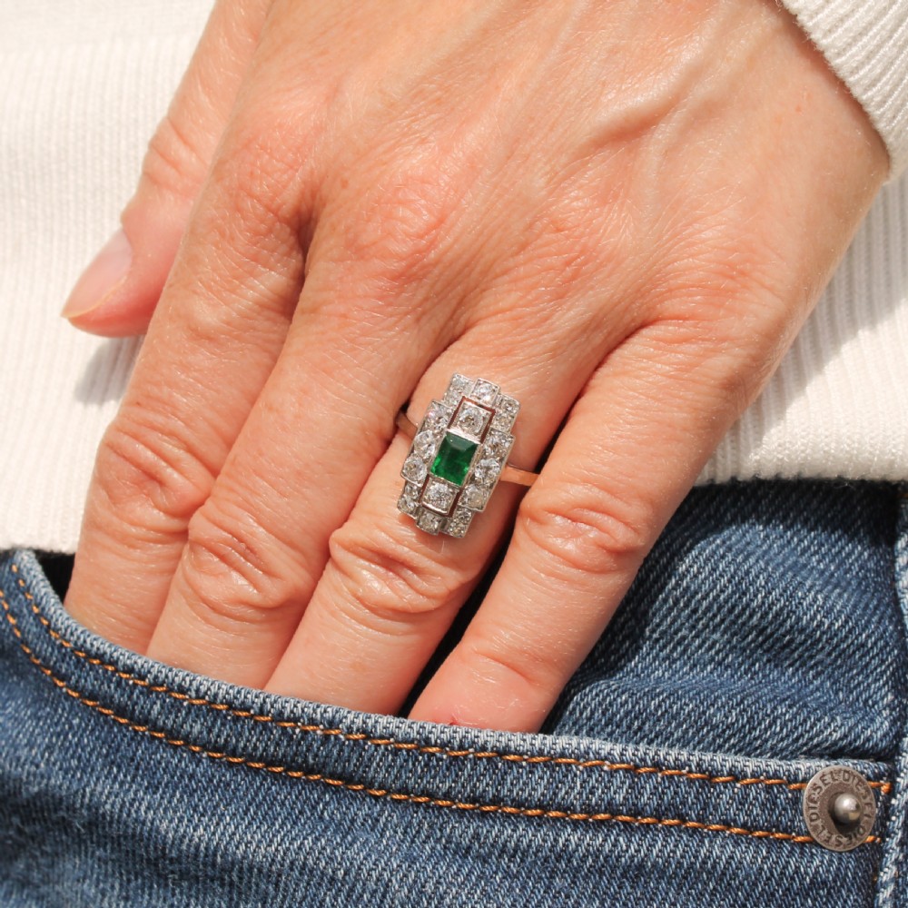 An Art Deco platinum ring featuring a central rectangular step-cut green emerald surrounded by geometric rows of old-cut diamonds. View VII