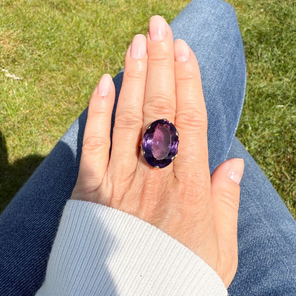 A mid-century rose gold solitaire ring featuring a prominent oval-cut purple amethyst gemstone secured by multiple claw settings. View VII