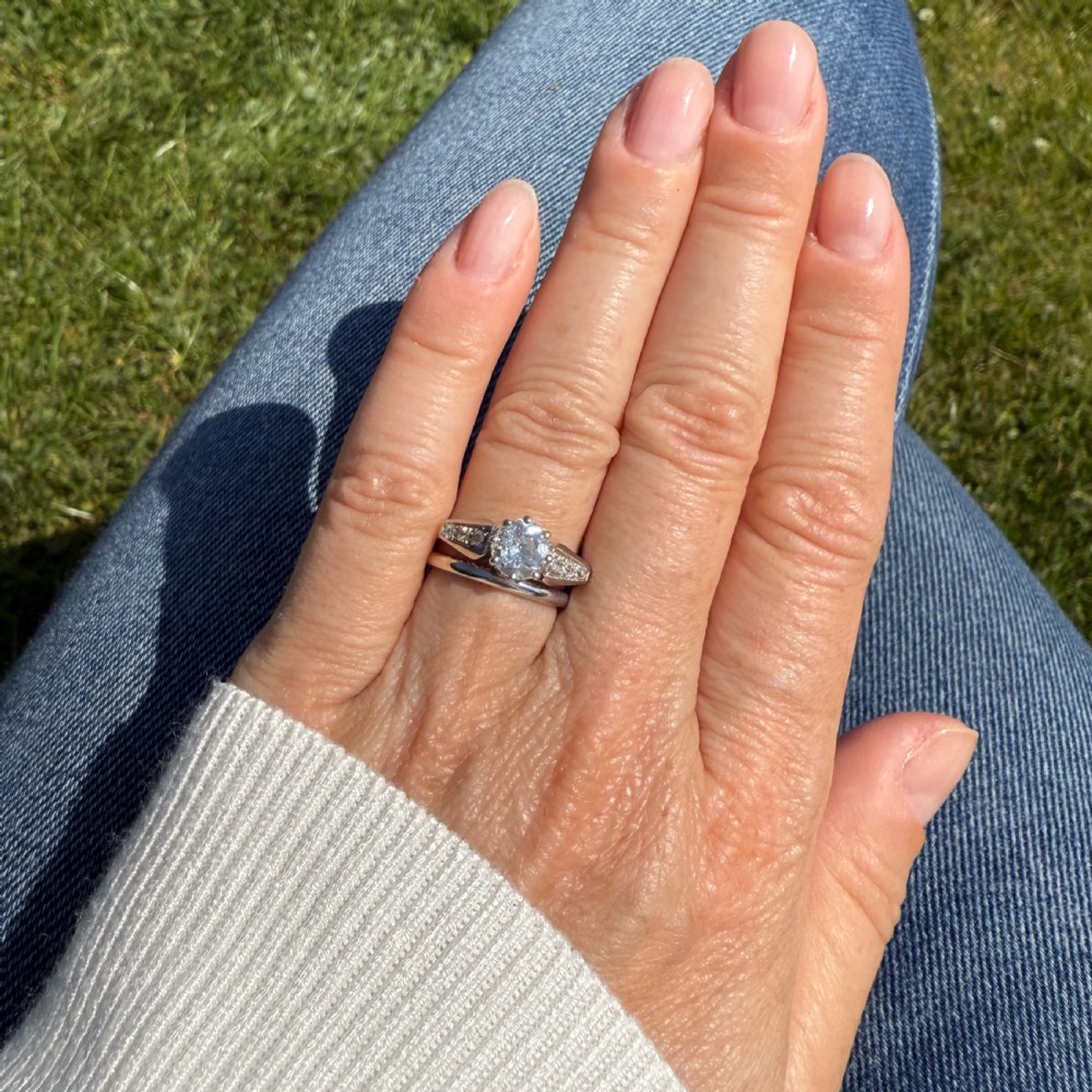 An Art Deco diamond engagement ring featuring a central round old European cut diamond set in platinum with geometric, diamond-paved shoulders and millegrain detailing. View VI