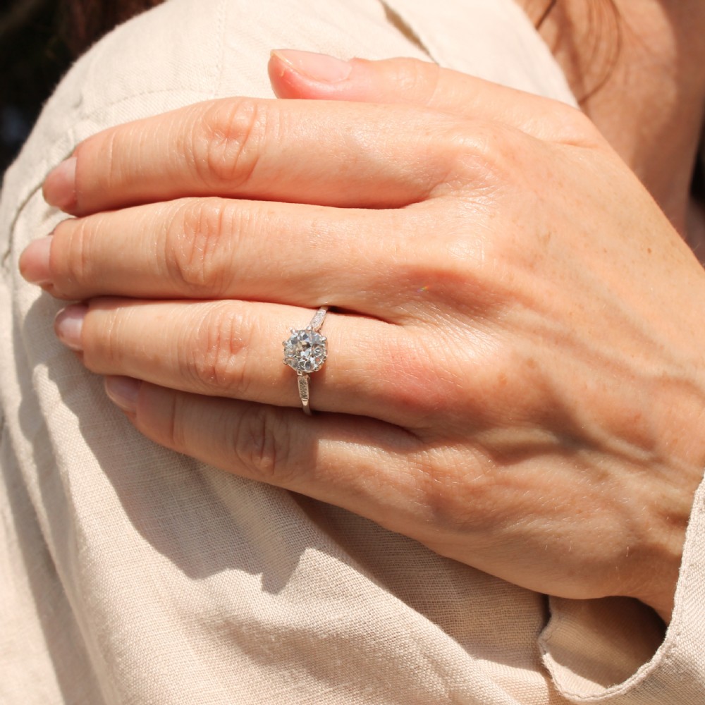 A mid-century platinum engagement ring featuring a central round old-cut diamond in a multi-claw setting with milgrain diamond shoulders. View VI