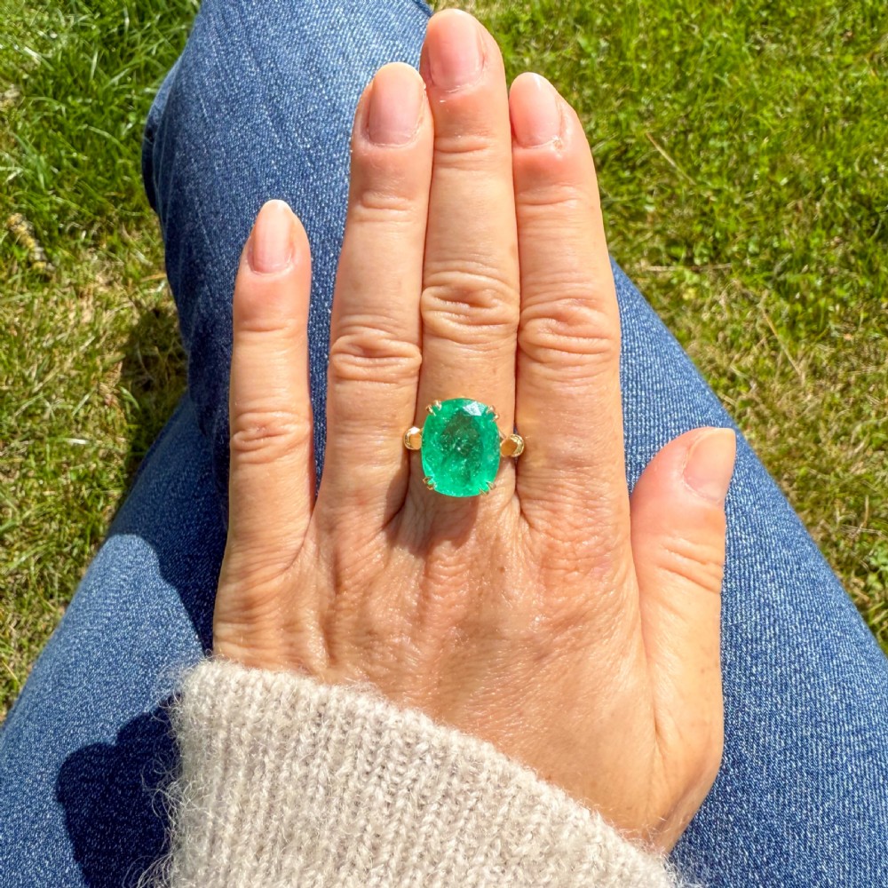 A mid-century yellow gold solitaire ring featuring a large cushion-cut green emerald secured with double claw settings. View VI