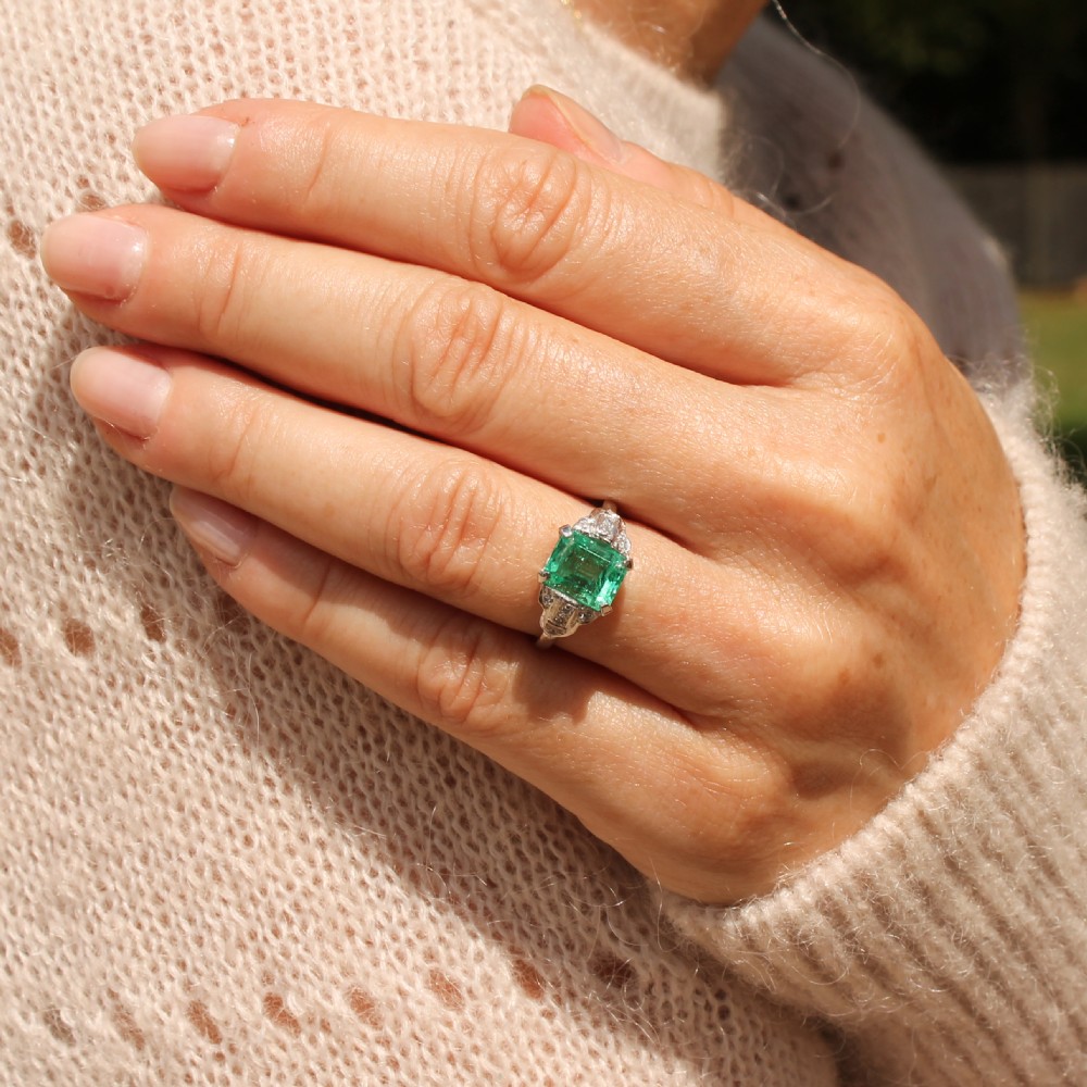 An Art Deco platinum ring featuring a central emerald-cut green gemstone flanked by geometric diamond-set shoulders. View VIII