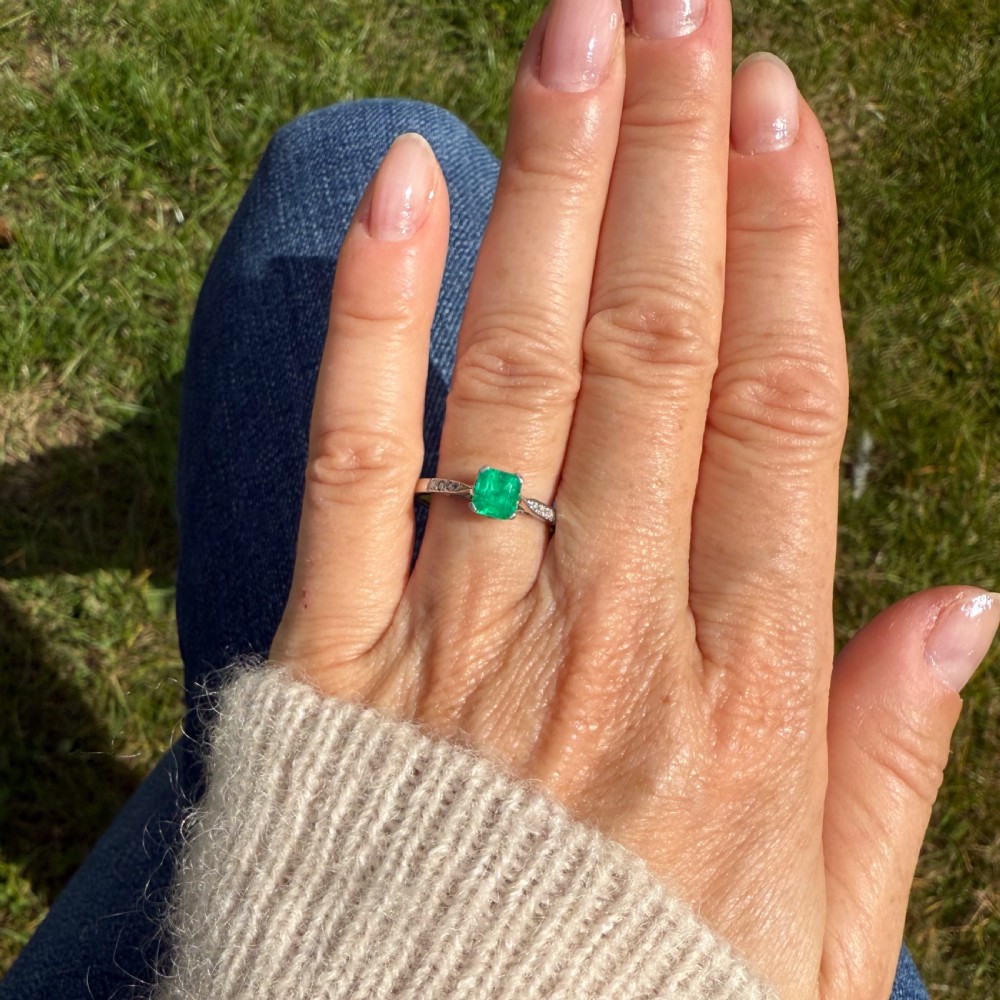 An Art Deco ring featuring a square-cut green emerald solitaire set in a platinum band with small diamond shoulders. View VI