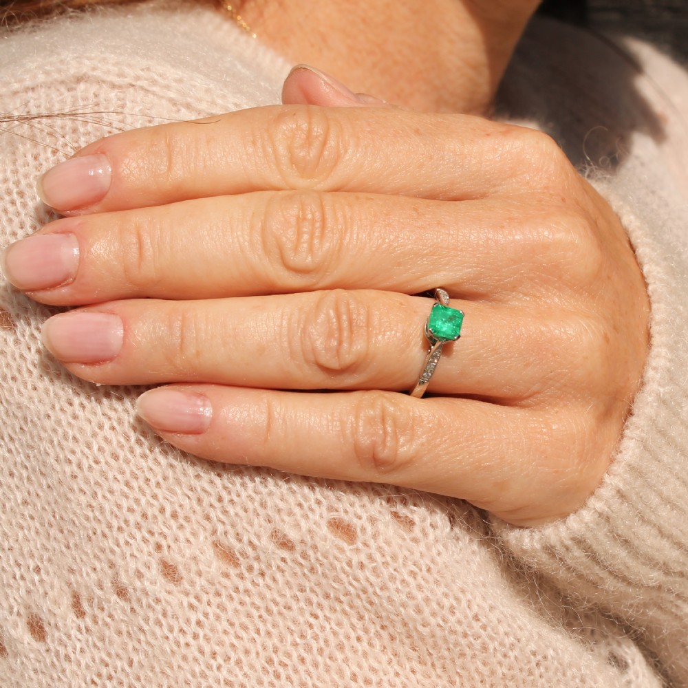 An Art Deco ring featuring a square-cut green emerald solitaire set in a platinum band with small diamond shoulders. View VII