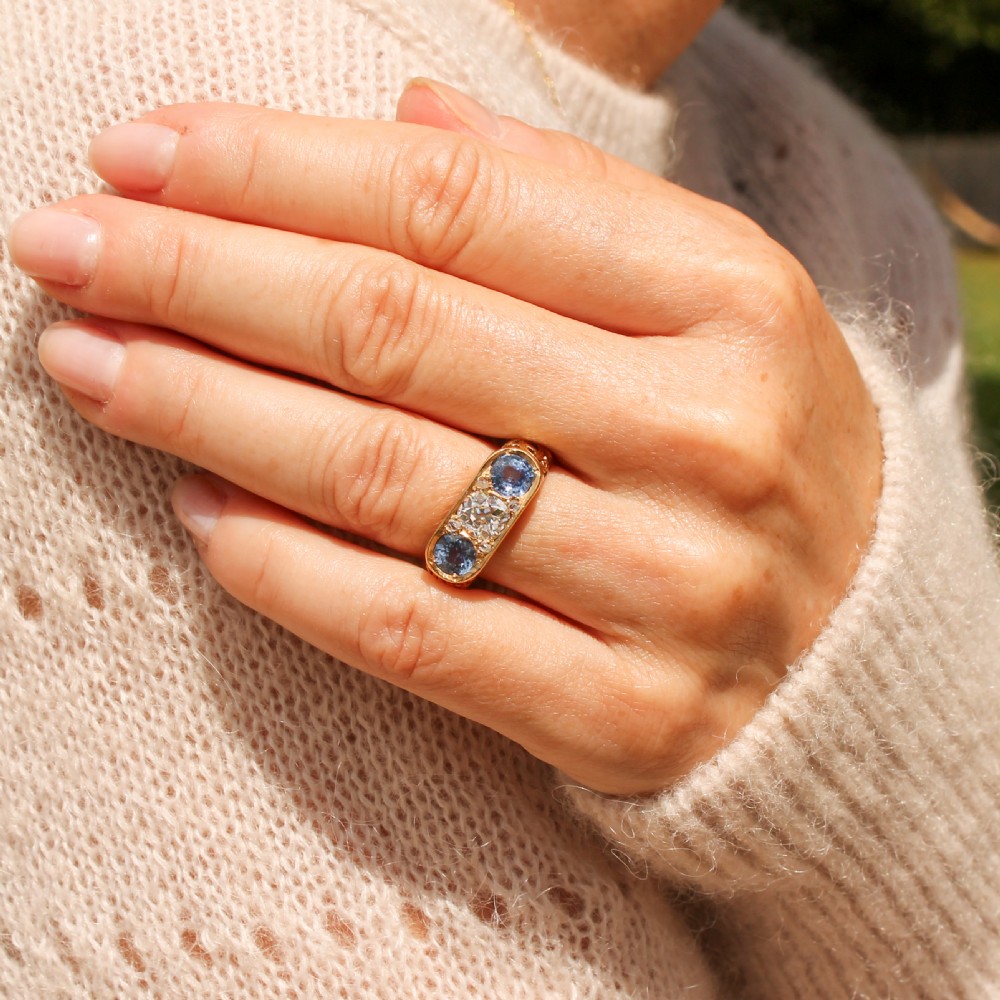 An Art Nouveau yellow gold ring set with a central round old cut diamond flanked by two blue sapphires within an openwork scrollwork gallery. View VIII