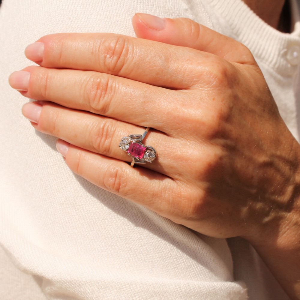 An Art Deco platinum ring featuring a central rectangular pink-red ruby flanked by round and baguette cut diamonds in an asymmetric setting. View II