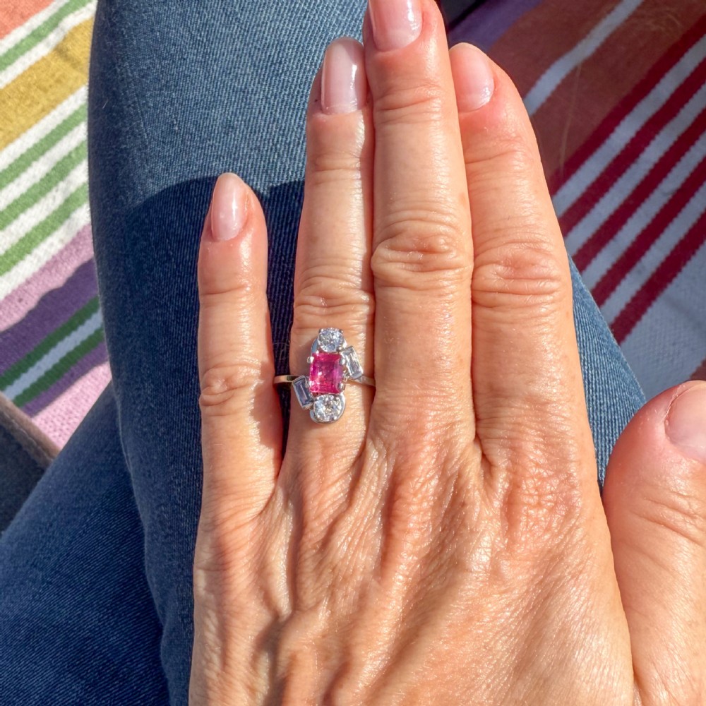 An Art Deco platinum ring featuring a central rectangular pink-red ruby flanked by round and baguette cut diamonds in an asymmetric setting. View VI
