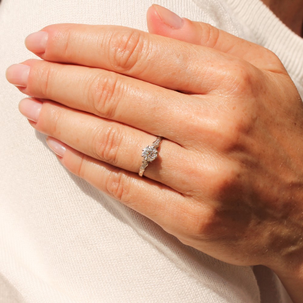 An Art Deco platinum engagement ring featuring a central round old cut diamond set in a coronet mount with detailed diamond shoulders. View VI