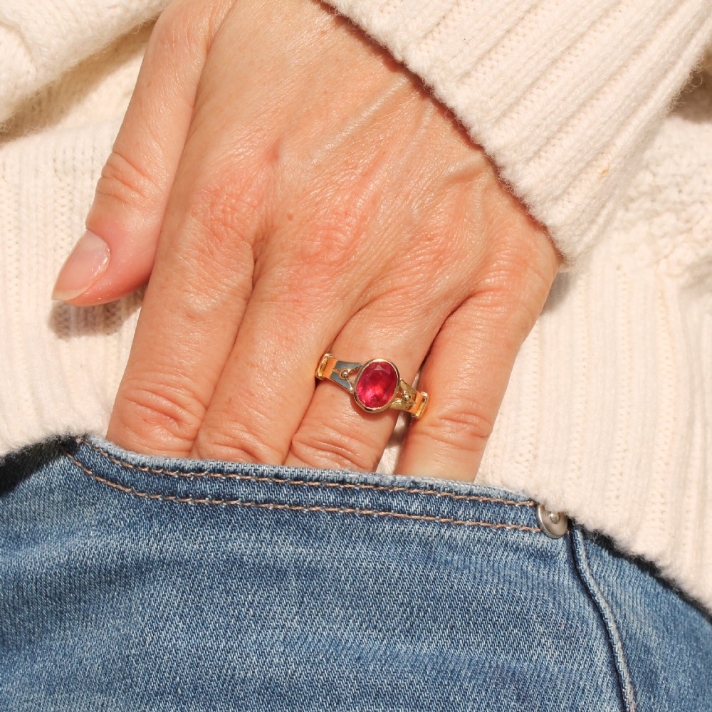 A Victorian yellow gold solitaire ring featuring a centrally set oval red ruby with decorated shoulders. View II