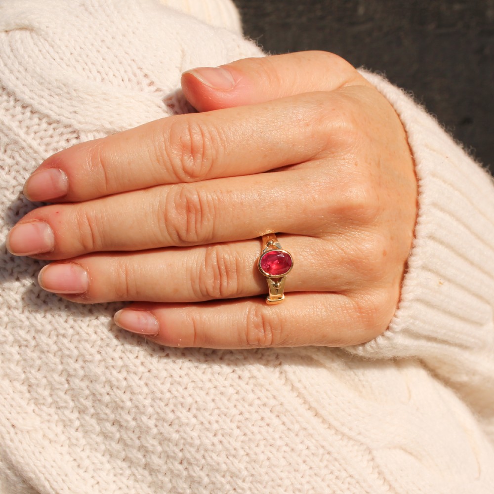 A Victorian yellow gold solitaire ring featuring a centrally set oval red ruby with decorated shoulders. View VII