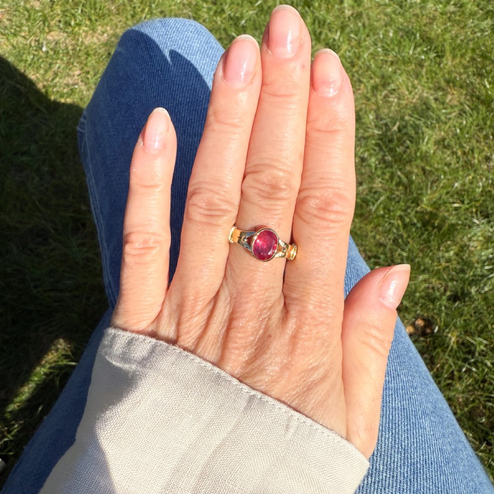 A Victorian yellow gold solitaire ring featuring a centrally set oval red ruby with decorated shoulders. View VIII