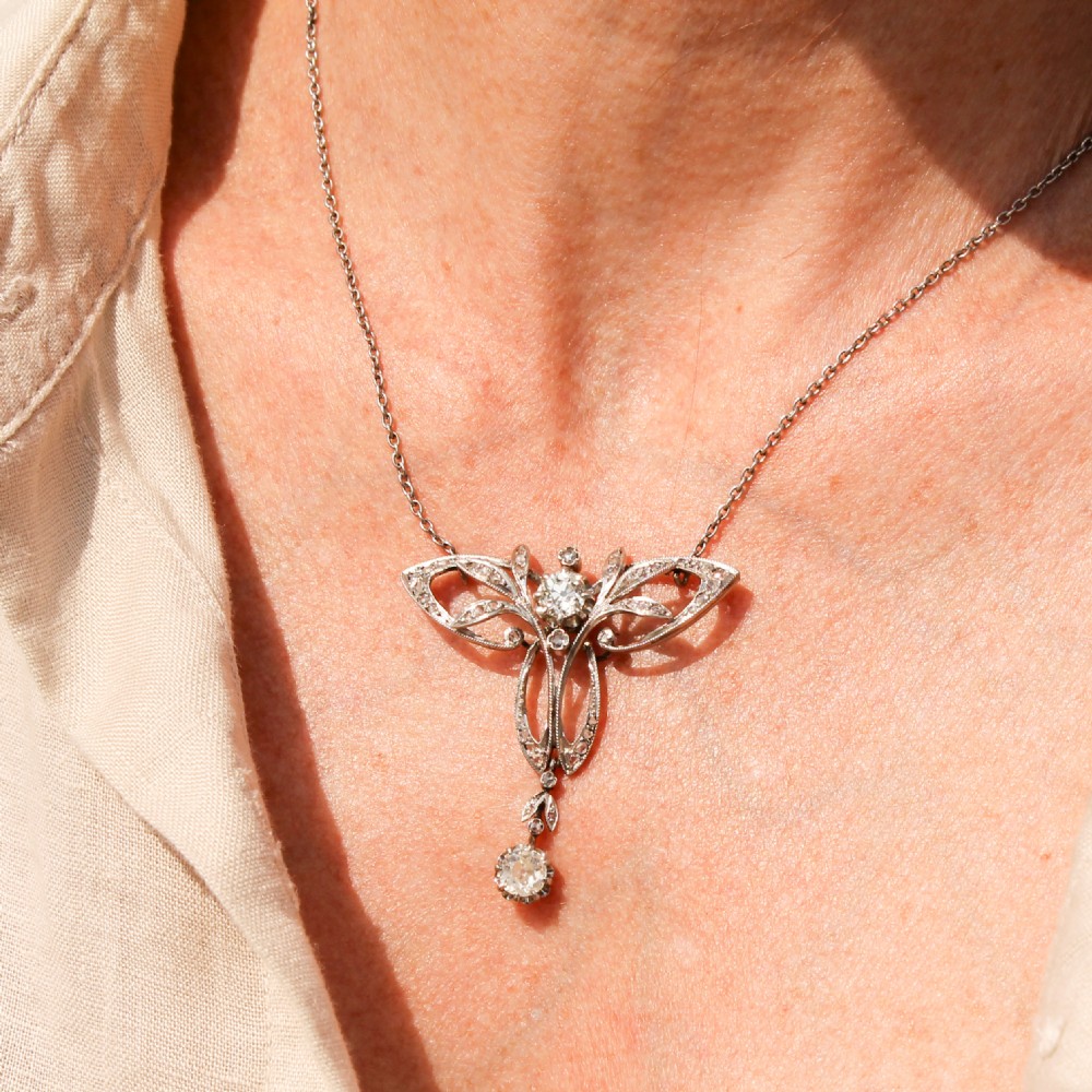 An Art Nouveau diamond pendant featuring openwork scrolling foliage set with diamonds and a dangling diamond drop suspended from a fine metal chain. View II