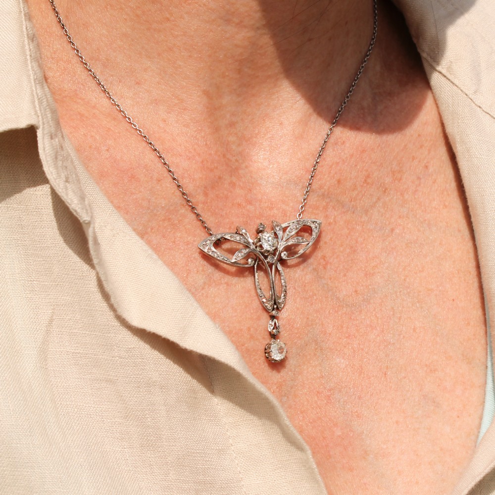 An Art Nouveau diamond pendant featuring openwork scrolling foliage set with diamonds and a dangling diamond drop suspended from a fine metal chain. View III
