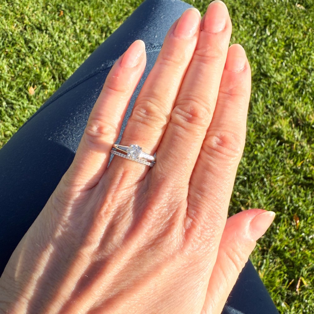 A vintage Art Deco diamond engagement ring featuring a round central stone with stepped baguette shoulders on a silver-coloured band. View VII