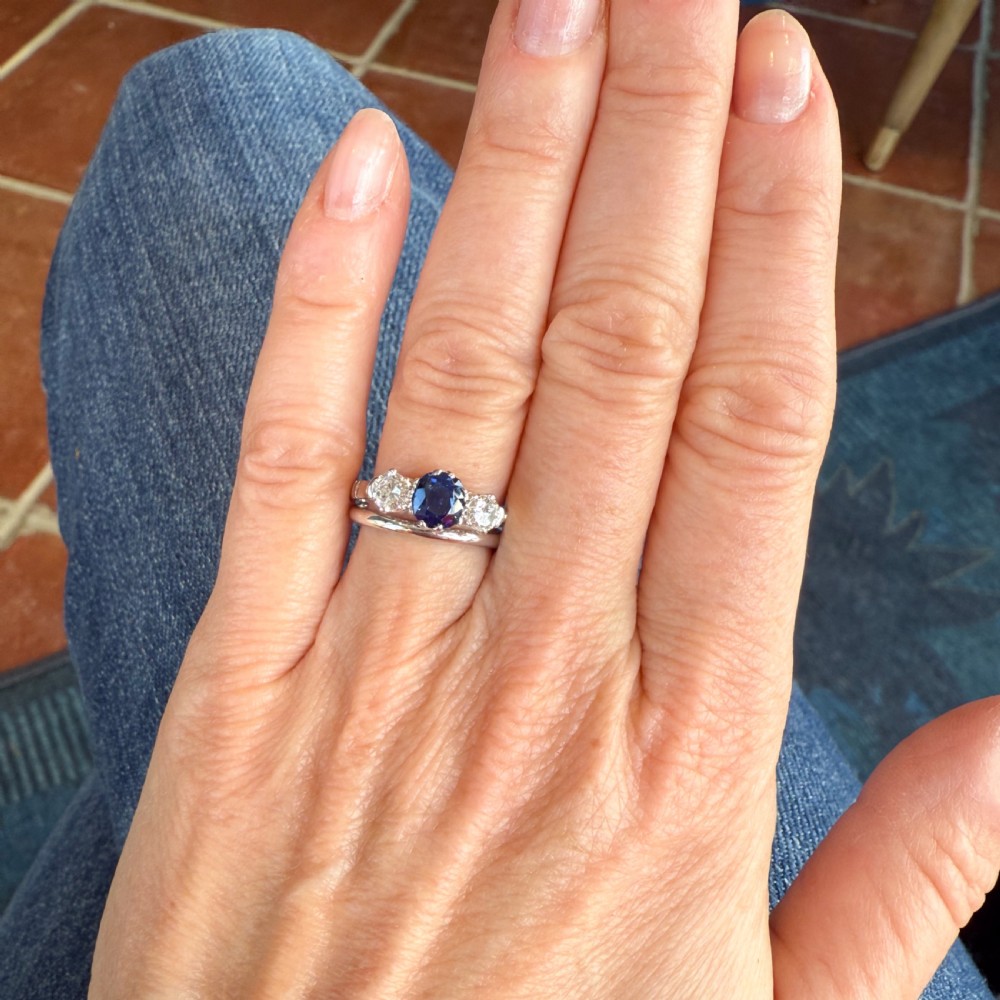 A platinum three-stone ring featuring a central blue sapphire set with claw prongs between two round brilliant-cut diamonds. View VII