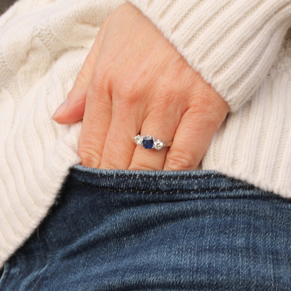 A platinum three-stone ring featuring a central blue sapphire set with claw prongs between two round brilliant-cut diamonds. View VIII