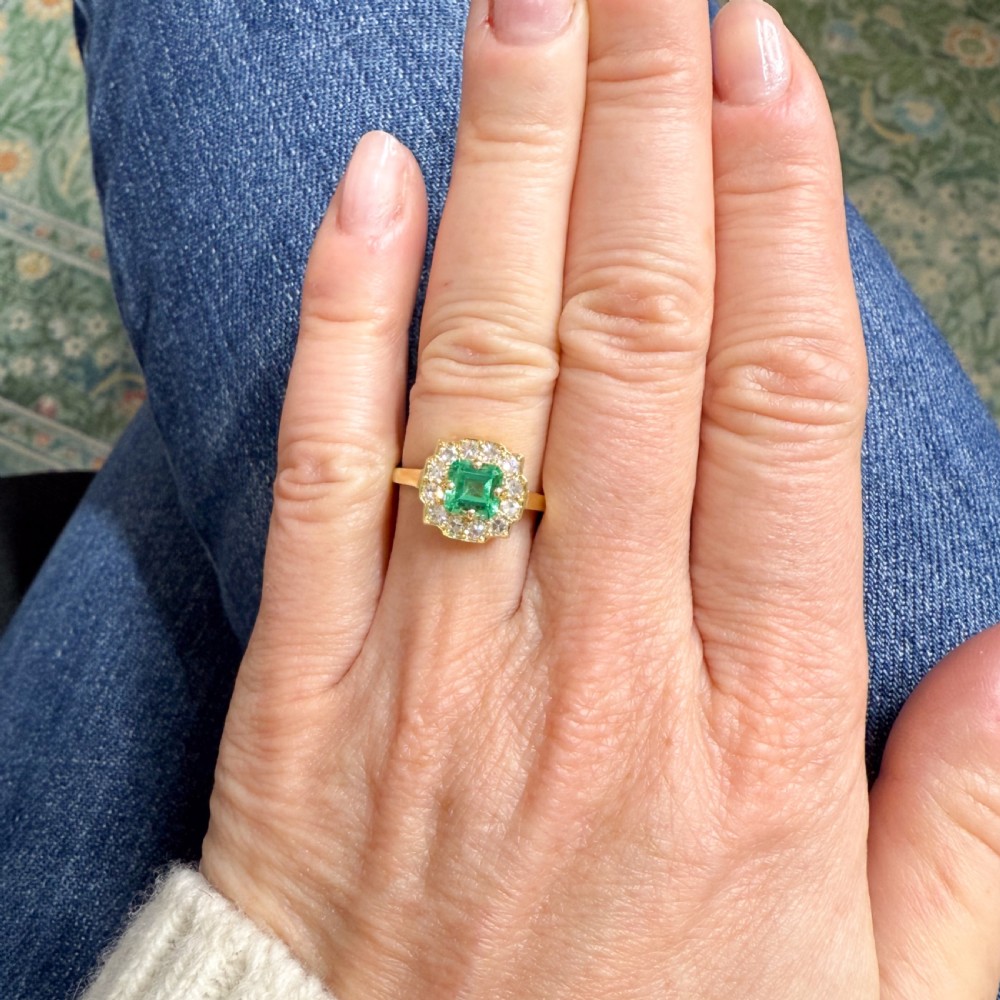 A yellow gold Art Deco cluster ring featuring a central square green emerald surrounded by a geometric halo of round diamonds. View II