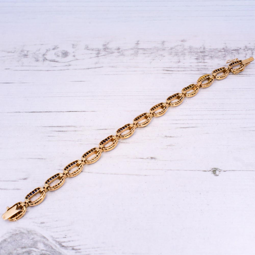 A yellow gold link bracelet set with channel-set blue sapphires and accented with small diamonds between each link. View VII