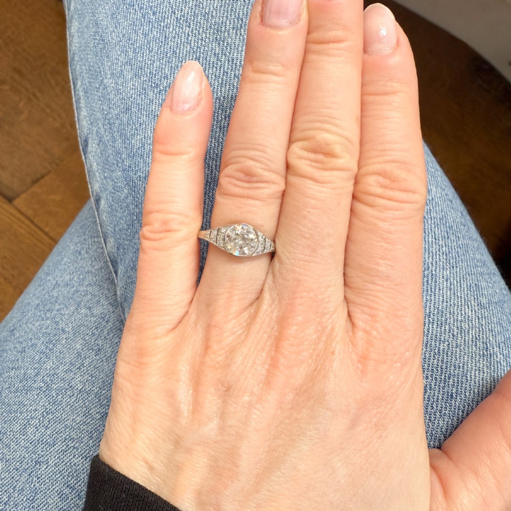 An Art Deco diamond ring featuring a central round old cut diamond set in platinum with small diamond accents along geometric shoulders. View VI