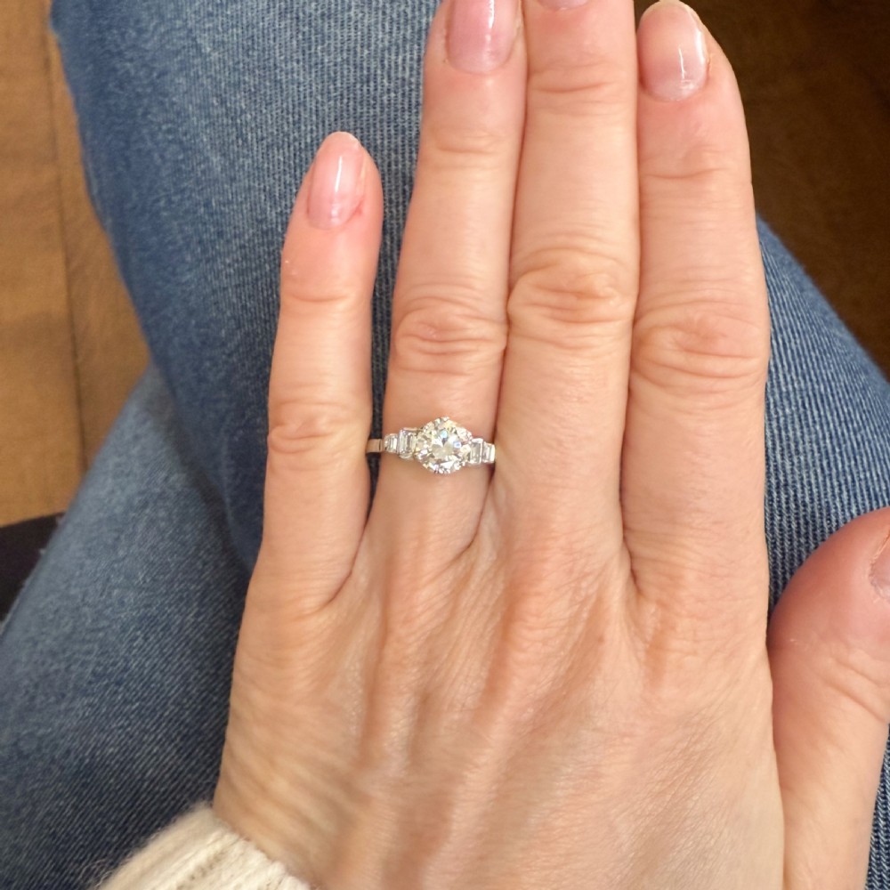 A platinum ring featuring a central round transitional cut diamond with baguette diamond shoulders. View VI
