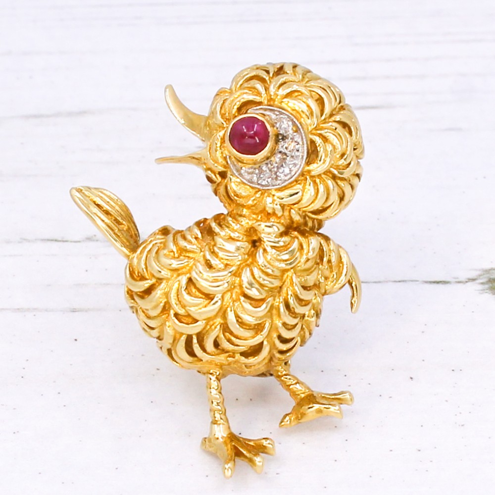 A textured yellow gold chick brooch featuring a cabochon ruby eye framed by small diamonds.