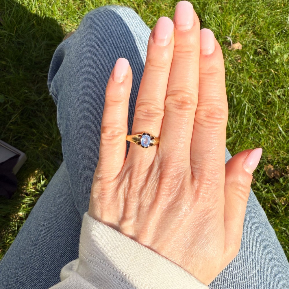 An antique yellow gold ring featuring a central oval pale blue sapphire set in claw mountings with hallmarks engraved inside the band. View VI