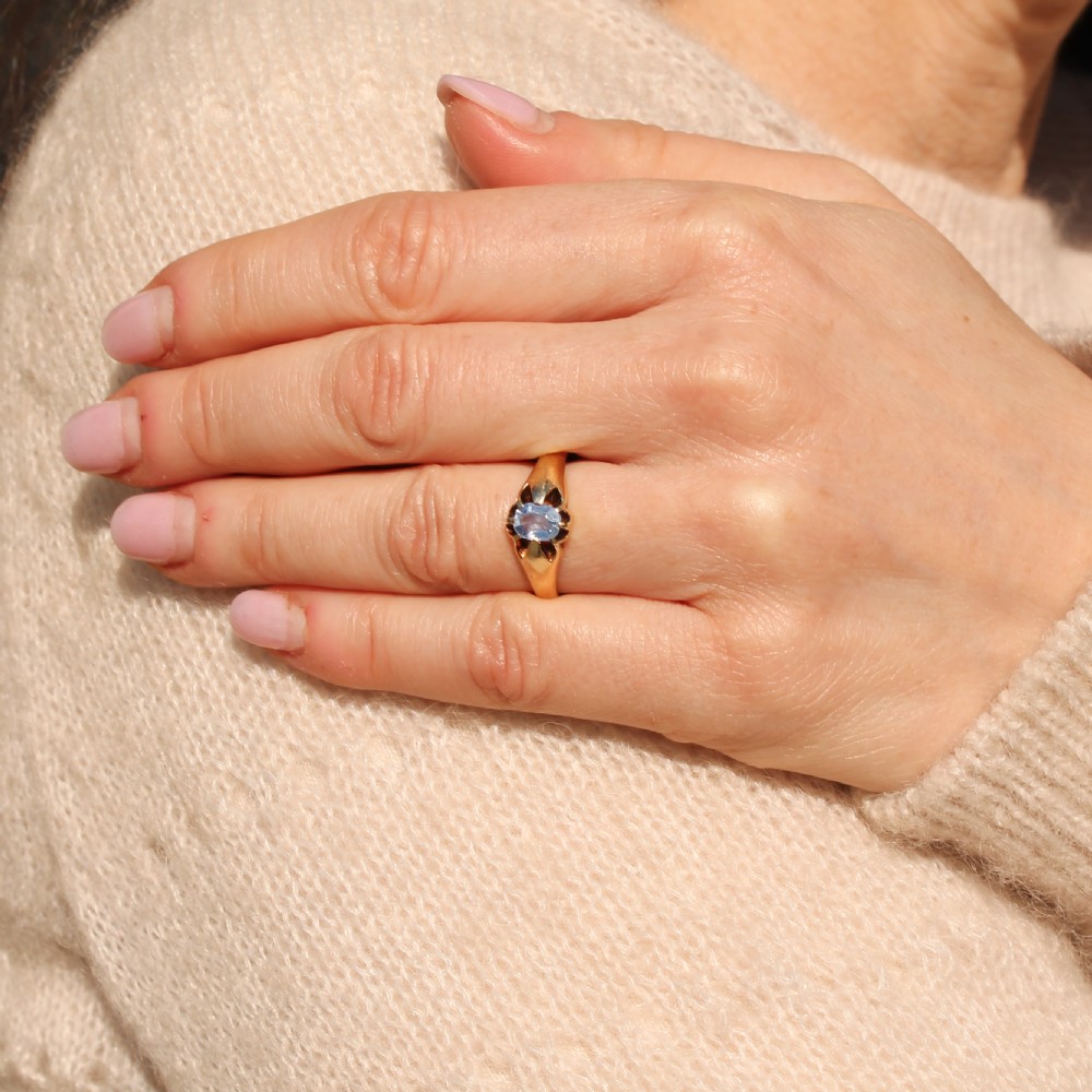 An antique yellow gold ring featuring a central oval pale blue sapphire set in claw mountings with hallmarks engraved inside the band. View VII
