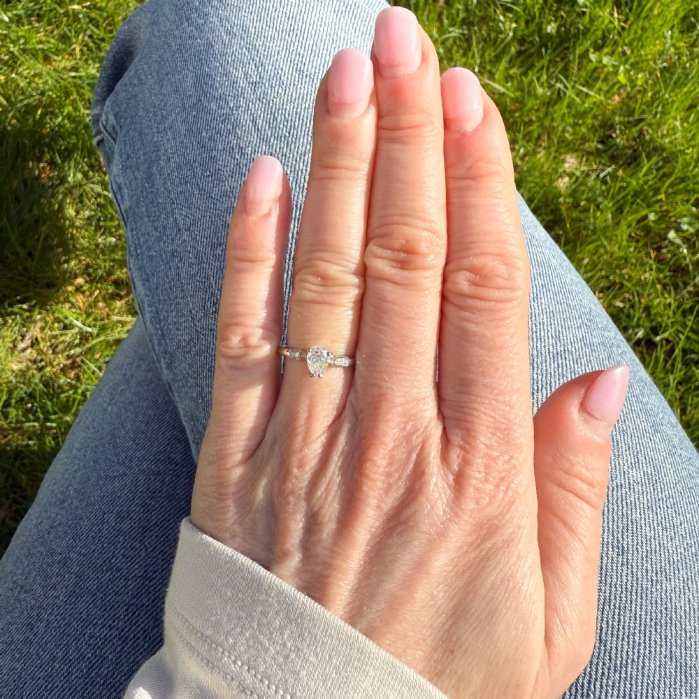A vintage platinum ring featuring a central pear-cut diamond in a prong setting with small diamond accents on the shoulders. View VI