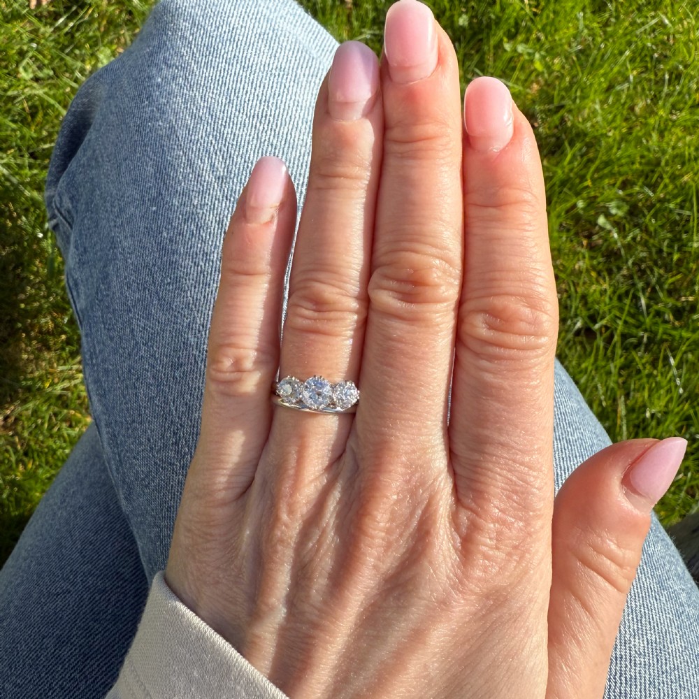 A vintage silver-toned ring featuring three round old cut diamonds set in a traditional trilogy claw mount. View VII
