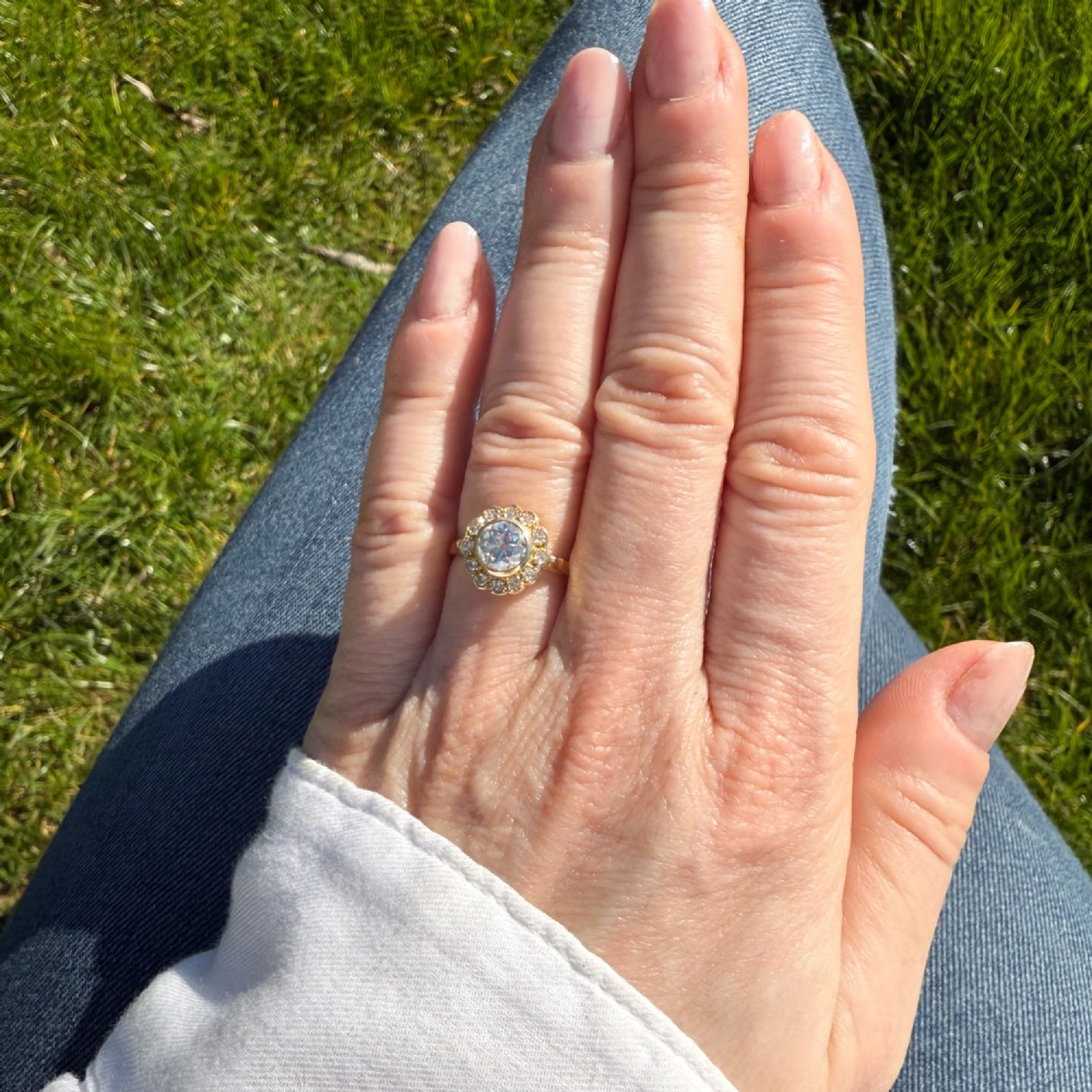 A yellow gold ring featuring a central old cut diamond in a bezel setting surrounded by a scalloped halo of smaller accent diamonds. View VI