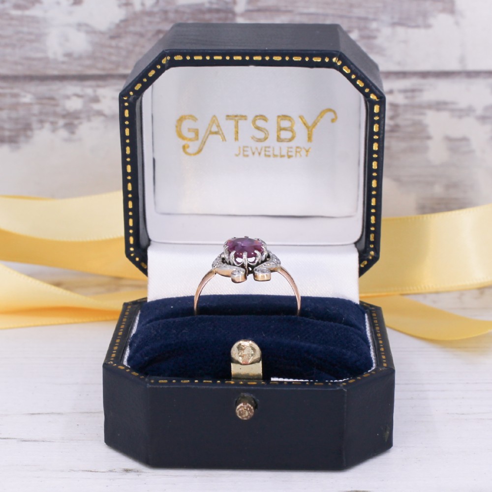 An antique Edwardian ring featuring an oval faceted pink sapphire surrounded by small diamonds set in scrollwork atop a yellow gold band. View IX
