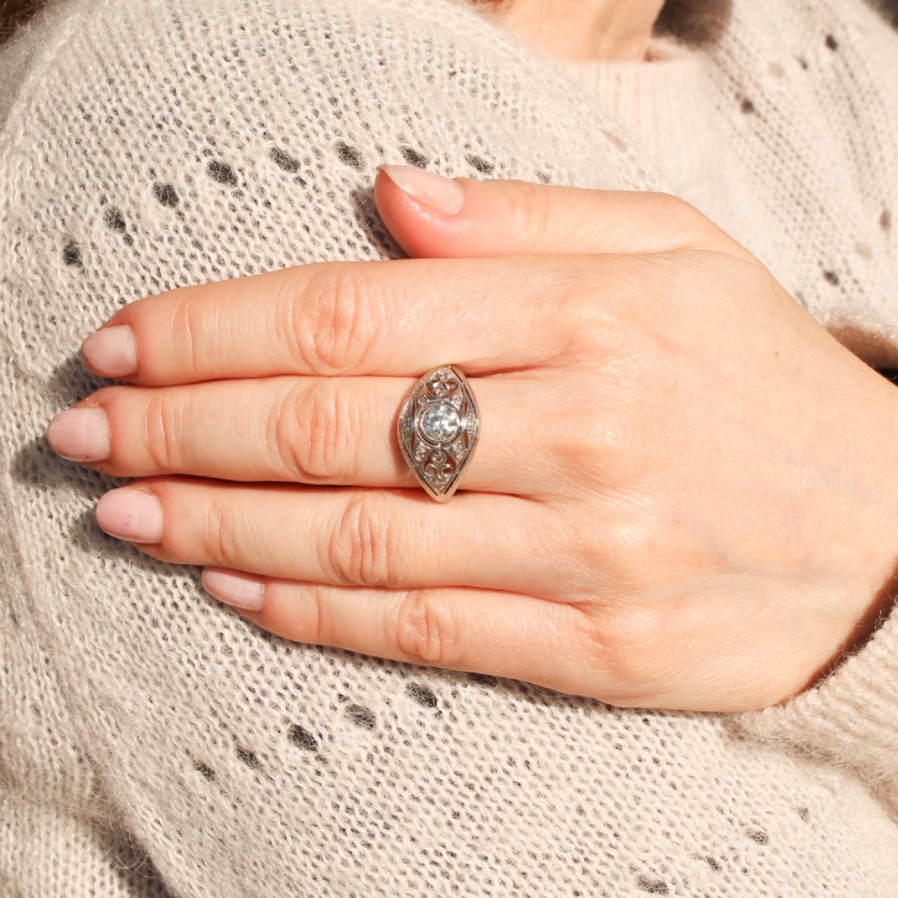 An Art Deco platinum ring featuring a central round old cut diamond in a bezel setting surrounded by pierced filigree scrollwork and small accent diamonds. View II