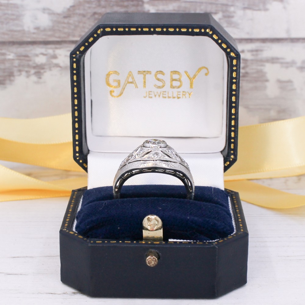 An Art Deco platinum ring featuring a central round old cut diamond in a bezel setting surrounded by pierced filigree scrollwork and small accent diamonds. View VIII