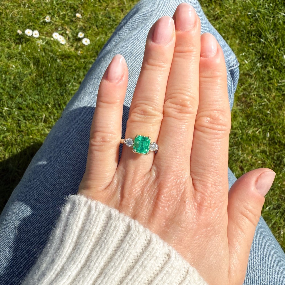 A vintage gold ring set with a rectangular central emerald-cut green gemstone and two flanking round brilliant diamonds. View VI