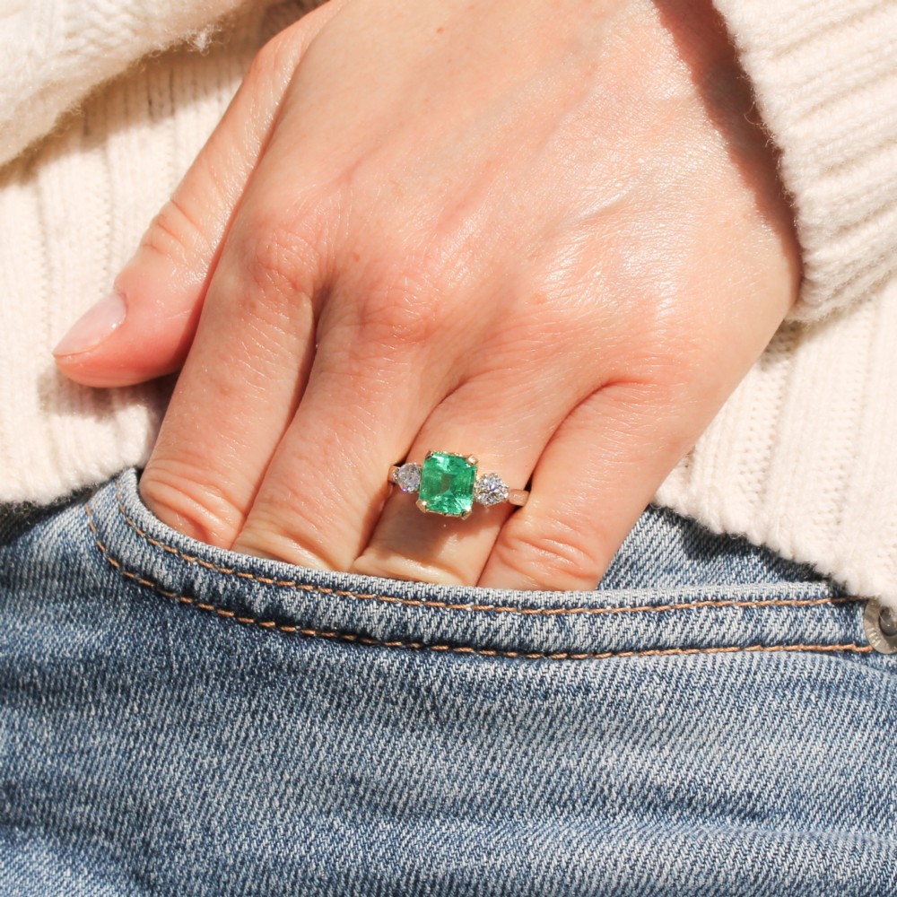 A vintage gold ring set with a rectangular central emerald-cut green gemstone and two flanking round brilliant diamonds. View VII