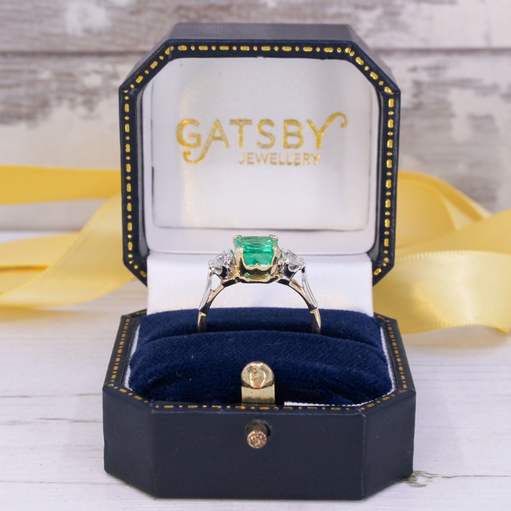 A vintage gold ring set with a rectangular central emerald-cut green gemstone and two flanking round brilliant diamonds. View IX