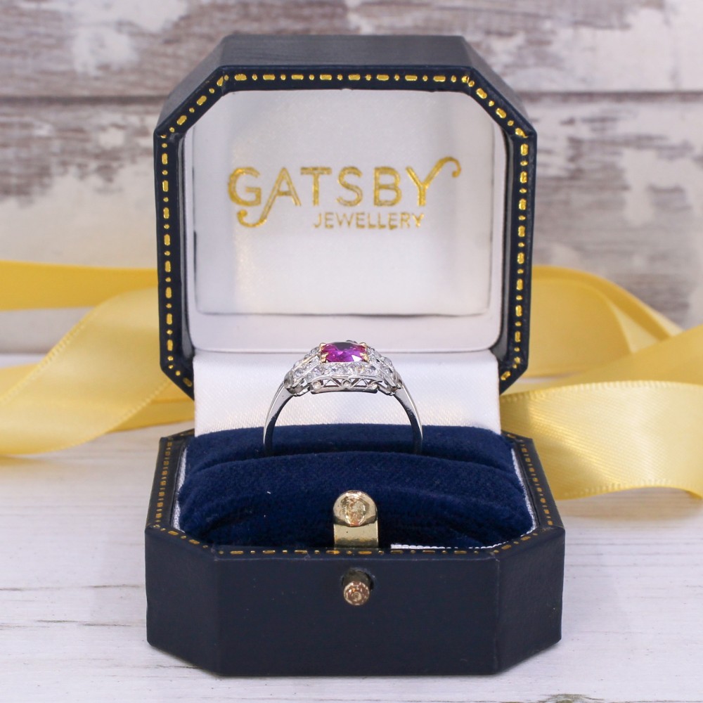An Art Deco platinum ring featuring an oval pink sapphire in a four-claw setting surrounded by a geometric halo of diamonds with milgrain detail. View IX
