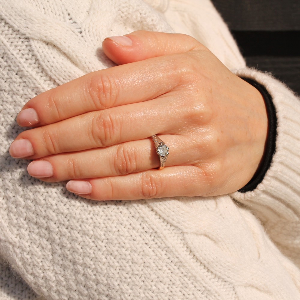 A vintage yellow gold solitaire engagement ring featuring a round brilliant cut diamond set in white metal claws with carved shoulders. View VI