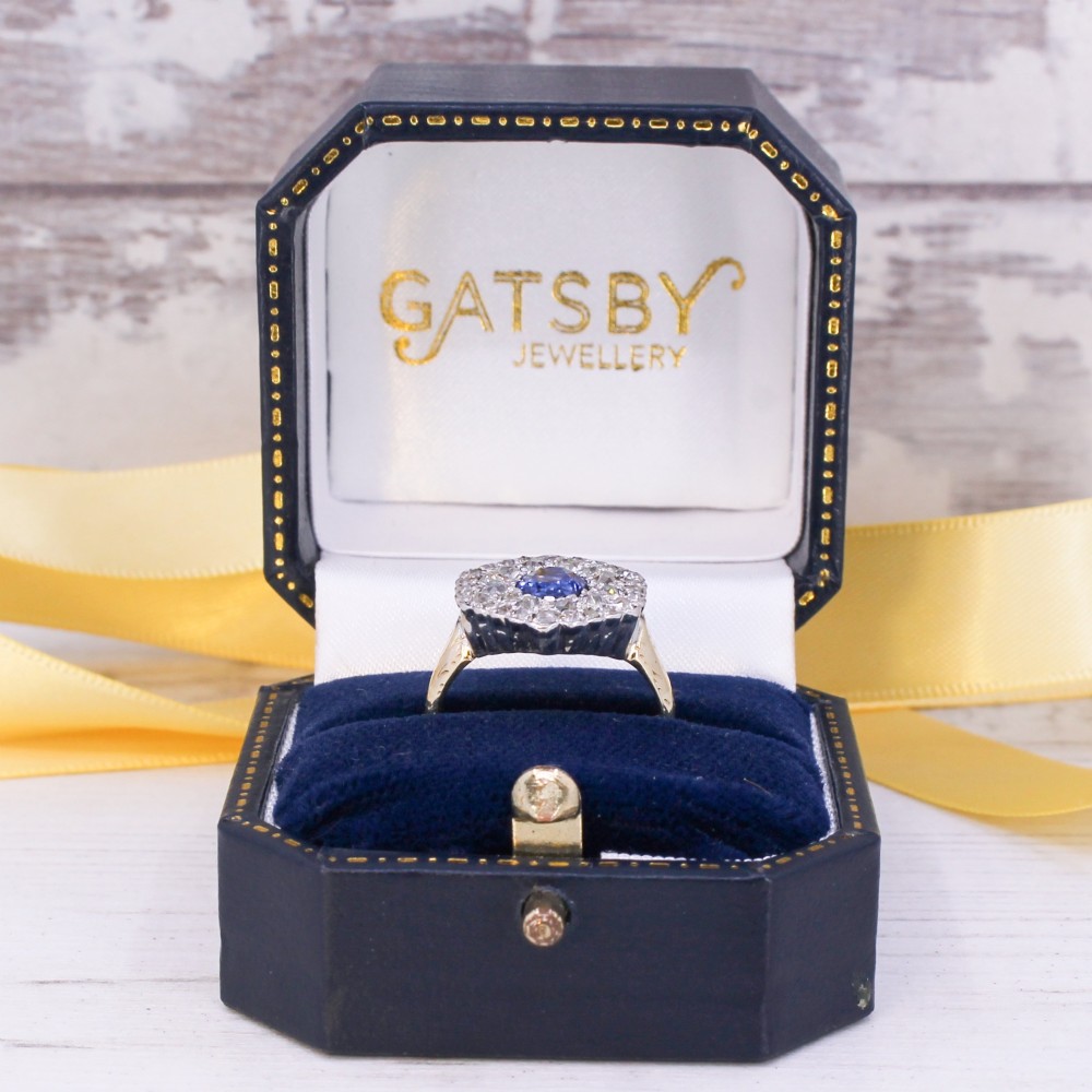 An oval blue sapphire surrounded by a double halo of diamonds set in a scalloped white metal mount on an engraved yellow gold band. View IX