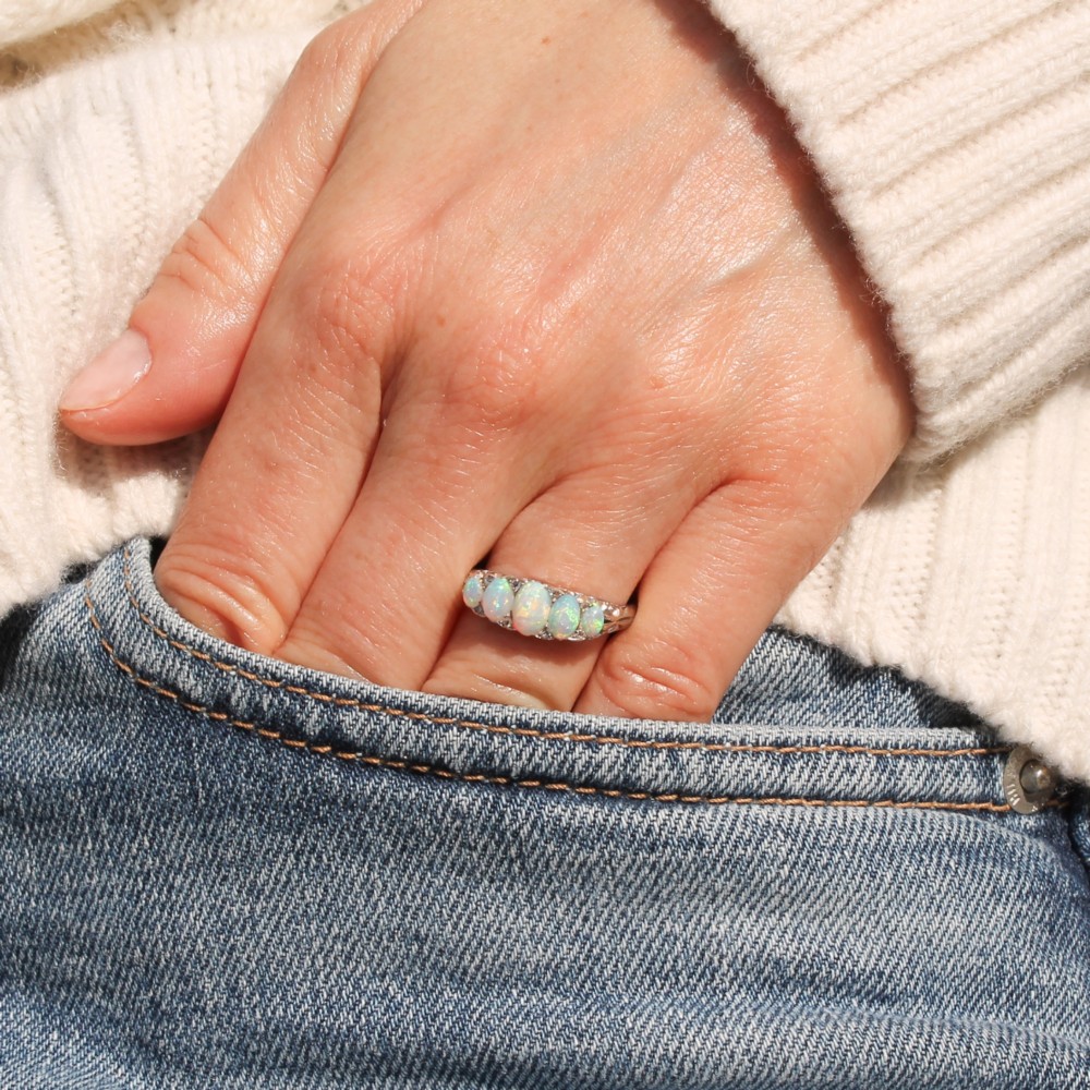 A white metal ring featuring five graduated oval cabochon opals set in a row across a decorative scrollwork setting. View II
