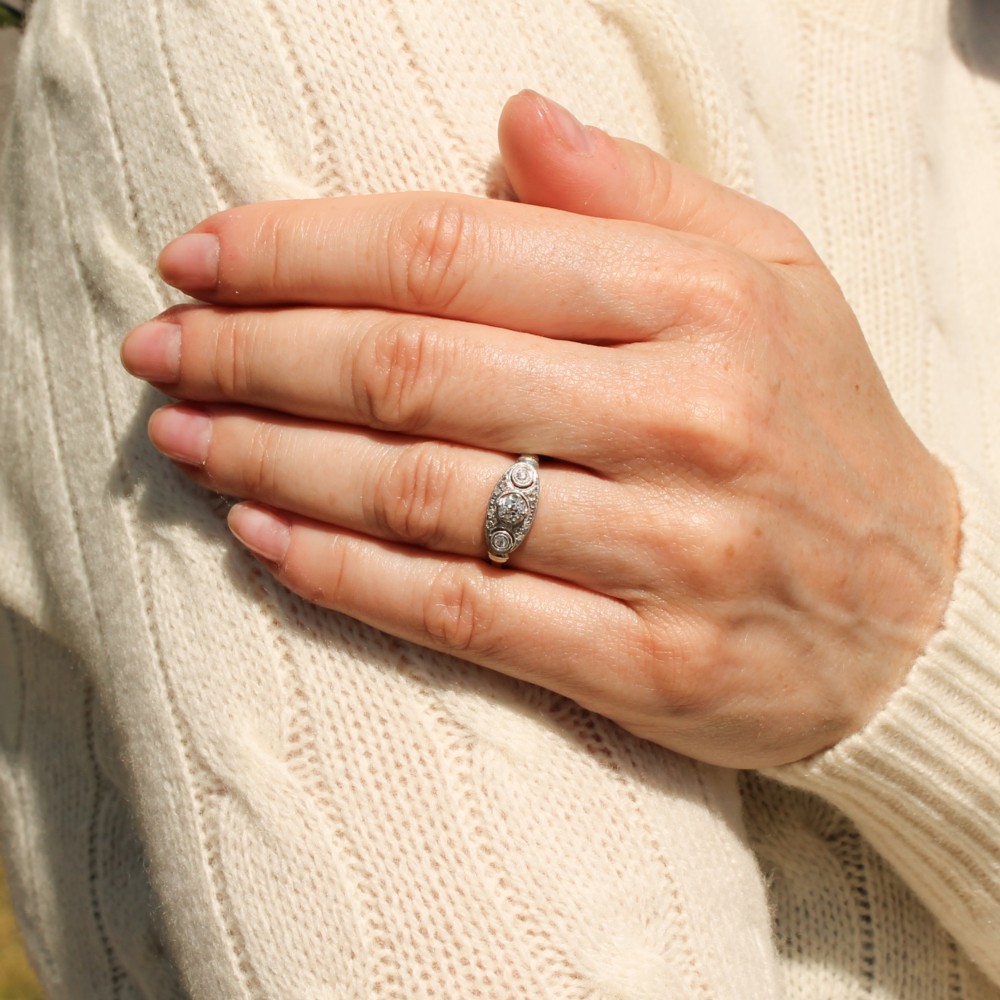 A vintage Art Deco white metal ring featuring a central old cut diamond flanked by two smaller diamonds in an elongated milgrained setting. View VII