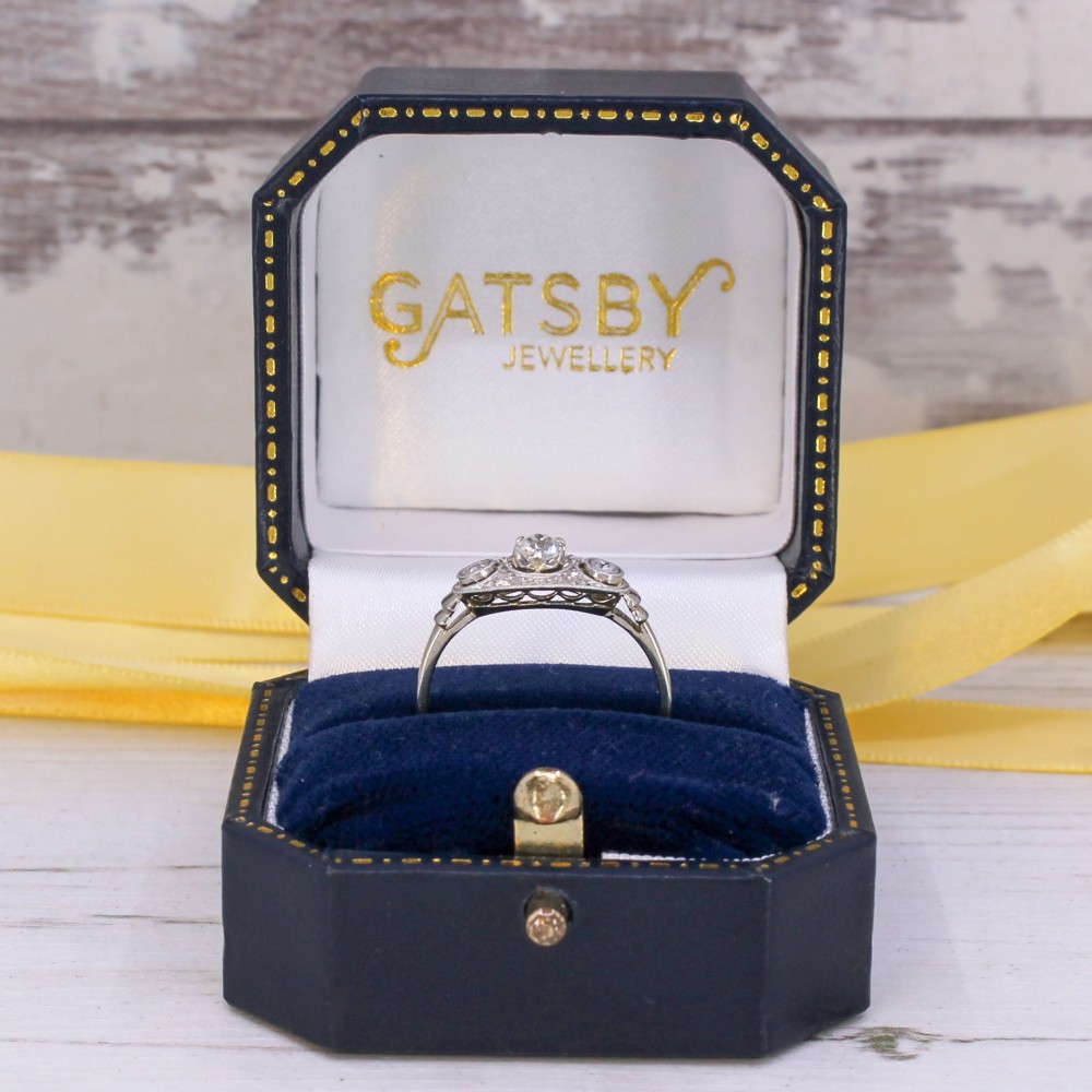 A vintage Art Deco white metal ring featuring a central old cut diamond flanked by two smaller diamonds in an elongated milgrained setting. View VIII