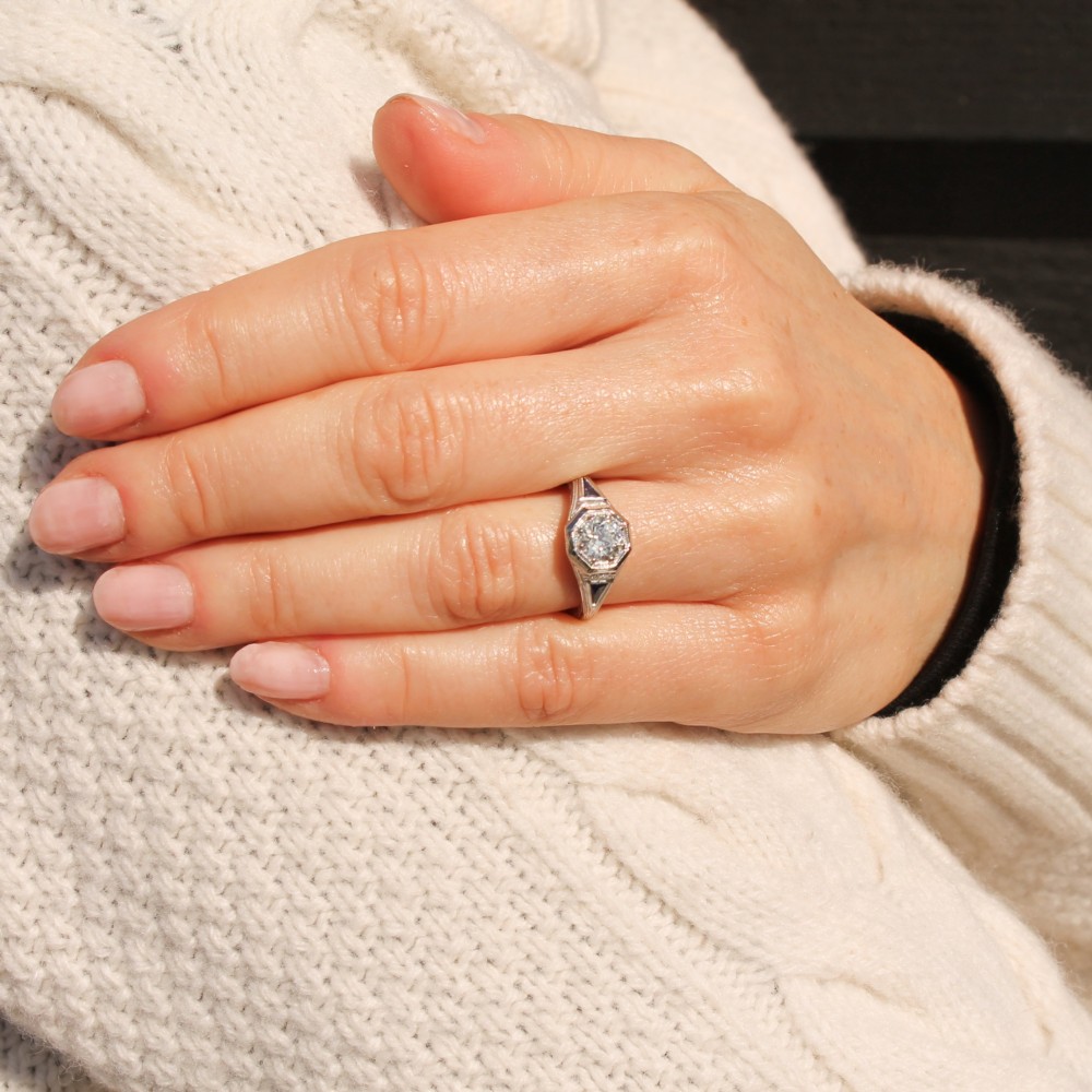 A white metal ring featuring a central old-cut diamond set within an octagonal bezel, flanked by triangular blue sapphires and fine engraved detailing along the band. View VII