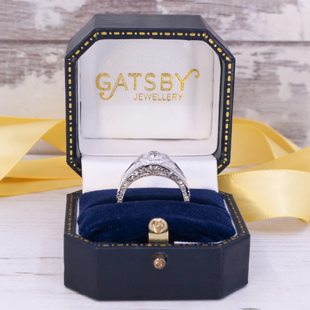 A white metal ring featuring a central old-cut diamond set within an octagonal bezel, flanked by triangular blue sapphires and fine engraved detailing along the band. View IX