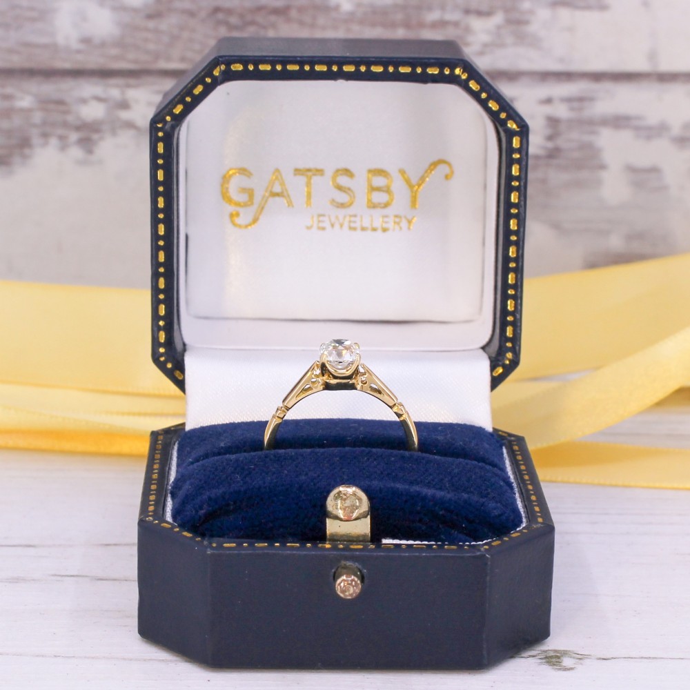A yellow gold solitaire ring featuring a central cushion shaped old cut diamond with geometric shoulder accents. View IX