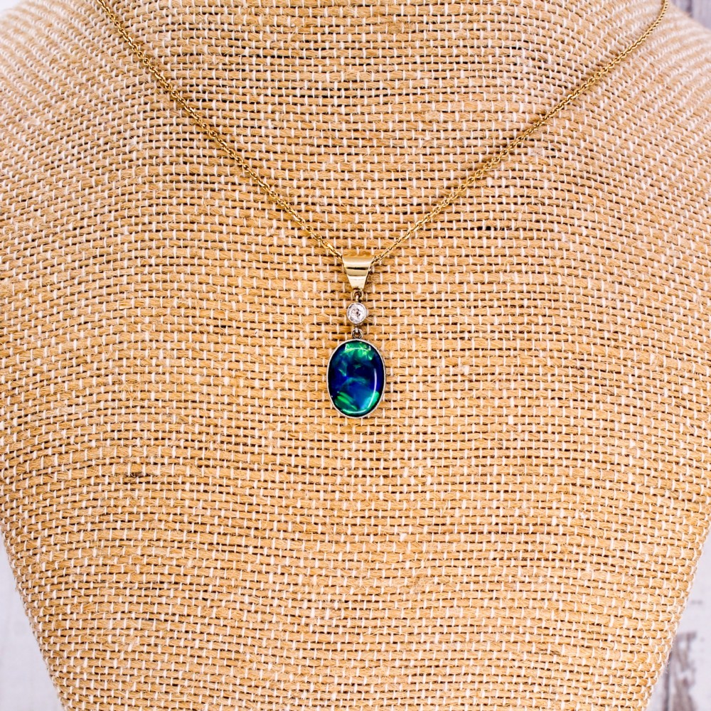 An Edwardian black opal and diamond pendant featuring an oval cabochon opal with blue and green play-of-colour mounted in gold below a bezel-set diamond. View V