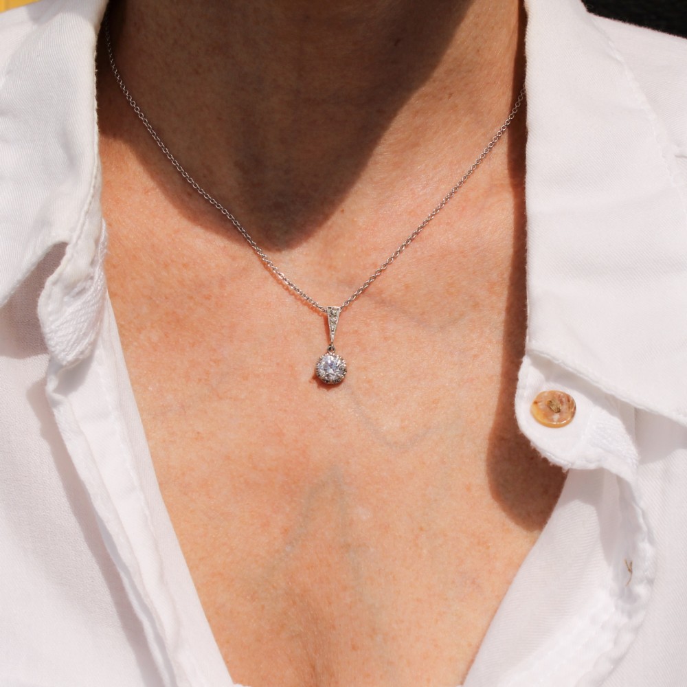 An Art Deco diamond pendant featuring a circular old cut diamond suspended from a linear diamond-set bale on a fine silver-toned chain. View III