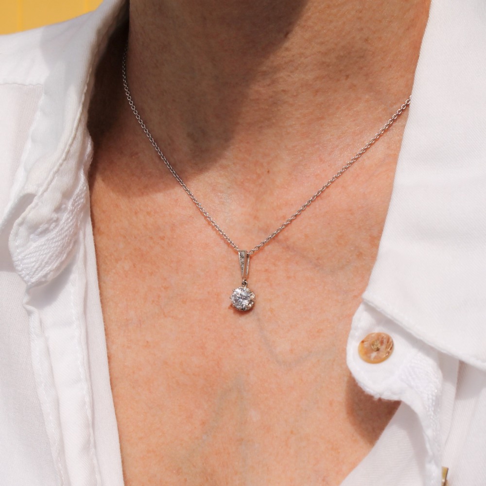 An Art Deco diamond pendant featuring a circular old cut diamond suspended from a linear diamond-set bale on a fine silver-toned chain. View IV
