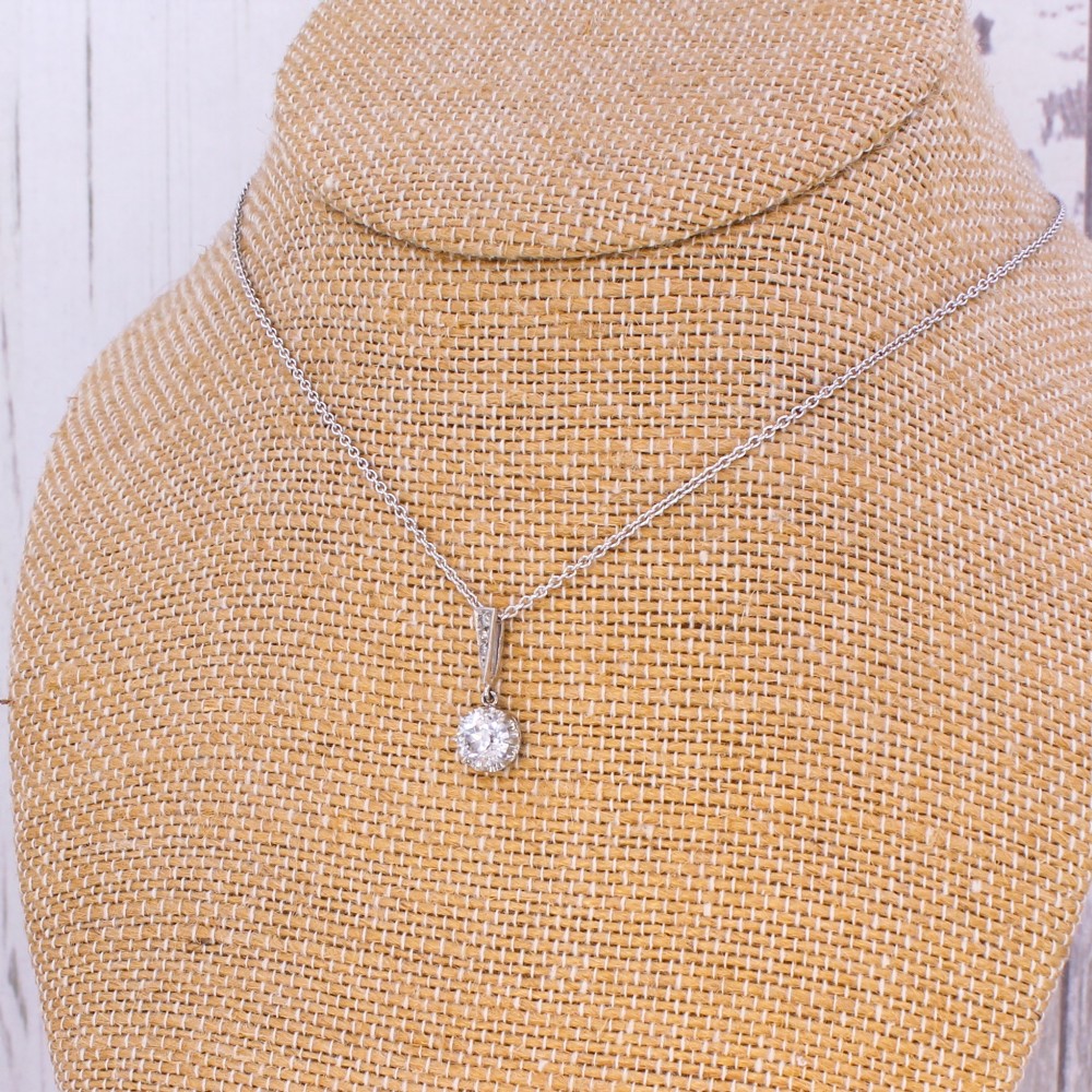 An Art Deco diamond pendant featuring a circular old cut diamond suspended from a linear diamond-set bale on a fine silver-toned chain. View V